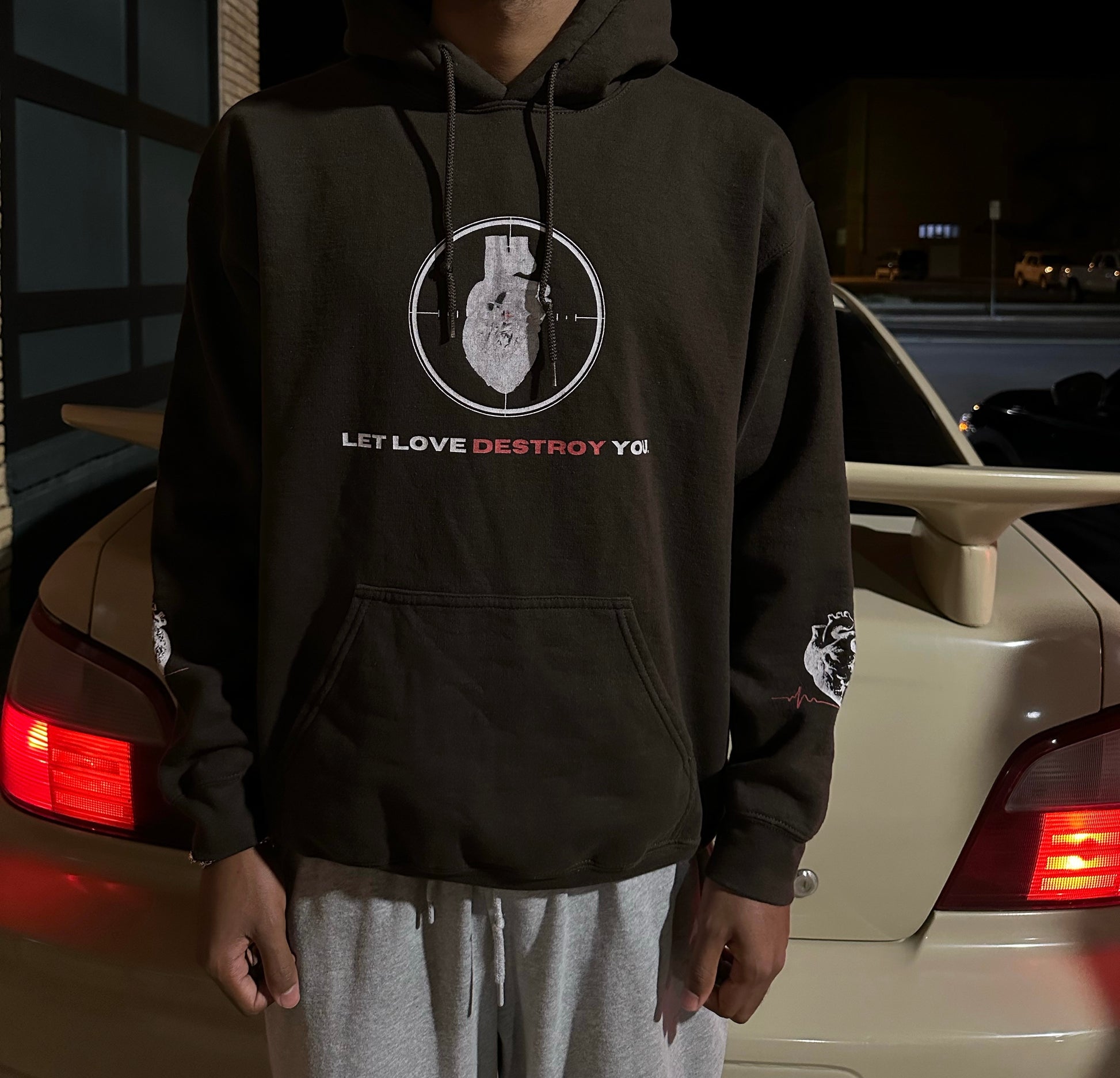 Front of brown Let Love Destroy You hoodie with anatomical heart target graphic and sleeve design worn at night.