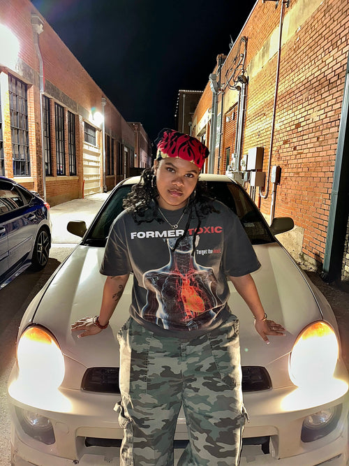 Model wearing Heat Scan Targeted Heart Tee with glowing red thermal heart graphic while leaning on car at night.